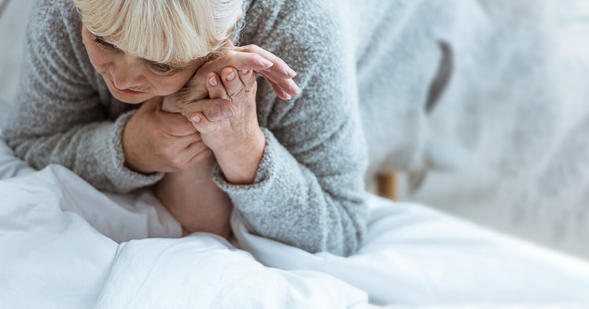 Person hält Hand der Angehörigen im Pflegebett