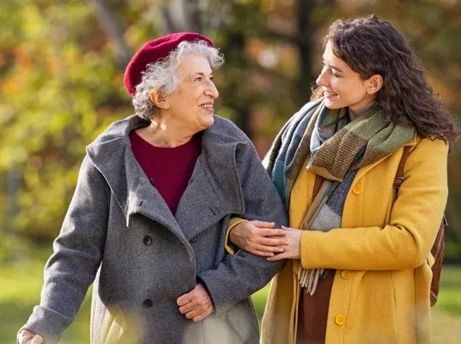 2 Frauen – alt und jung – gehen zusammen spazieren und lächeln sich an als Symbolbild für Lebensqualität im Alter