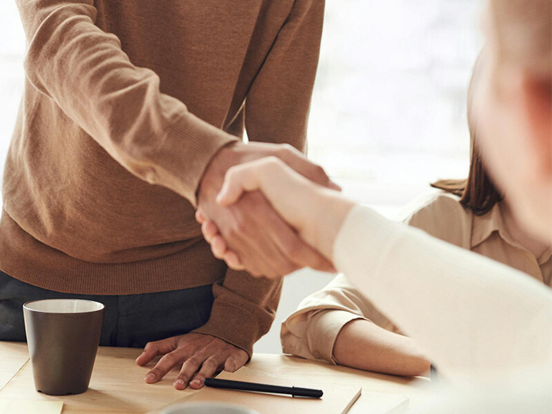 Zwei Personen geben sich in einem Büro über einem Tisch die Hand, was Fairness und professionelle Zusammenarbeit symbolisiert.