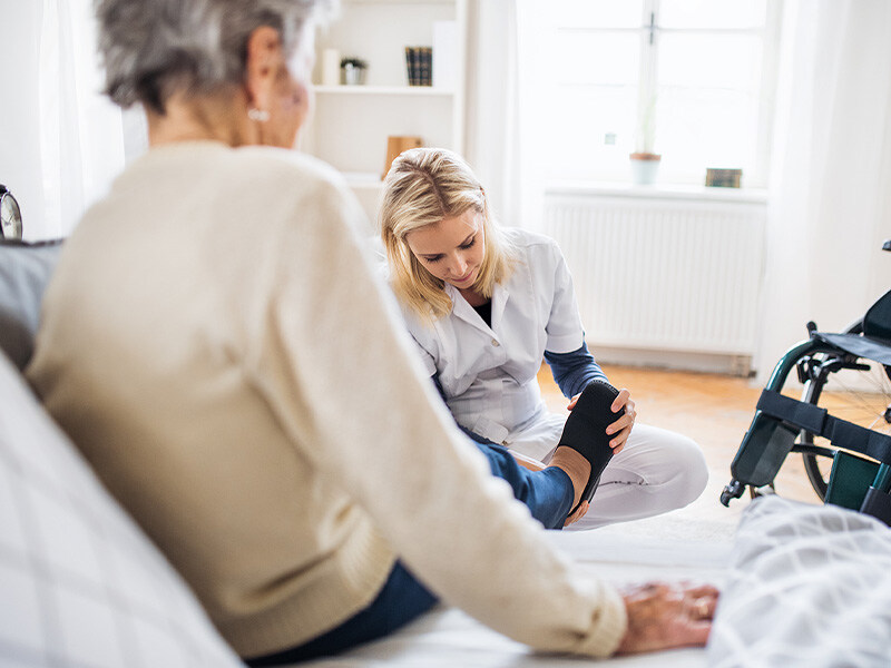 Private Spitex-Mitarbeiterin zieht älterer Patienten zu Hause Schuhe an.