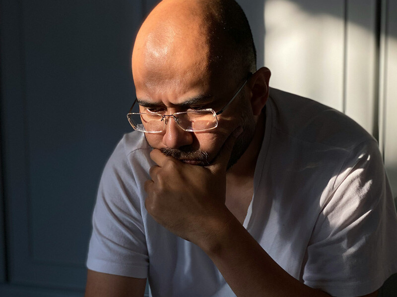 Nachdenklicher Mann mittleren Alters mit Brille in einem Sonnenlicht durchfluteten Raum, symbolisiert Reflexion und Sorgen um die geistige Gesundheit.