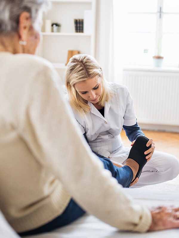 Private Spitex-Mitarbeiterin zieht älterer Patienten zu Hause Schuhe an.